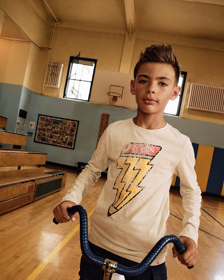 Young boy holding a bike handlebar in a gymnasium wearing a tee with a pencil design shaped like a lighning bolt 