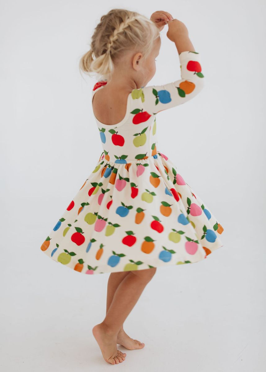 Child wearing a colorful dress with fruit pattern on a white background