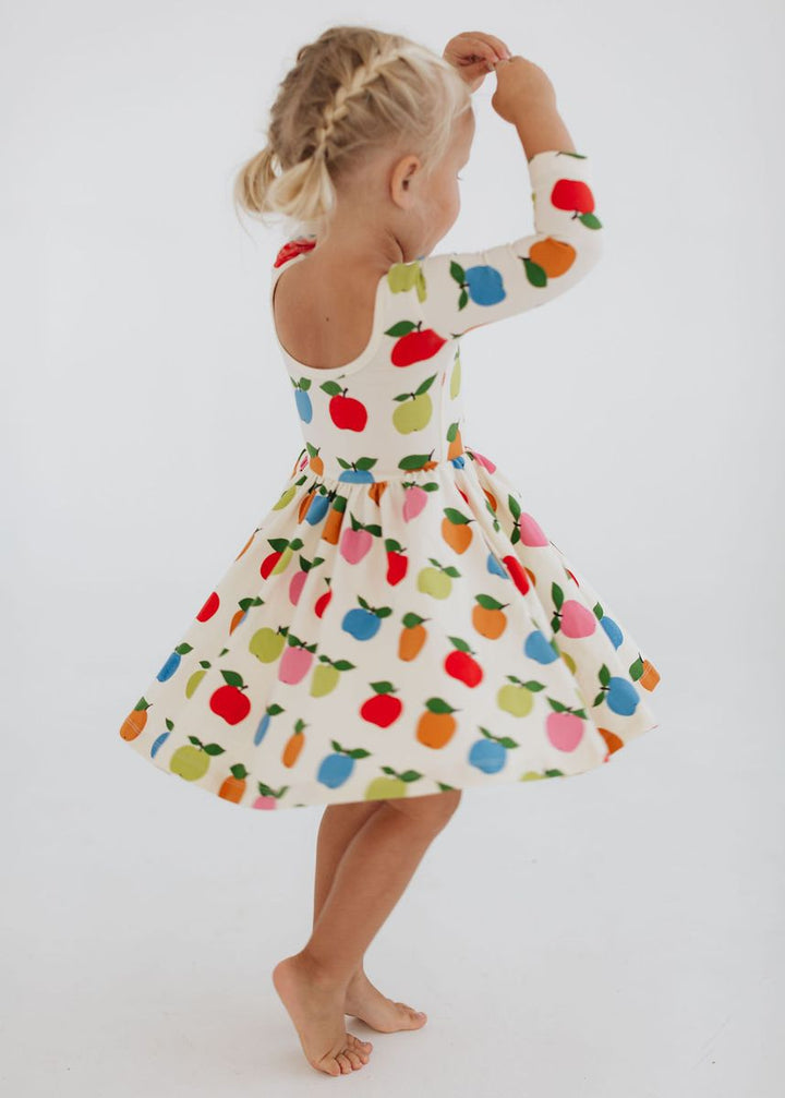 Child wearing a colorful dress with fruit pattern on a white background