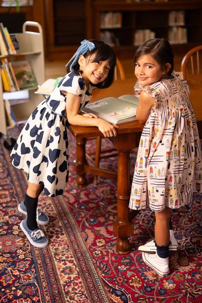 This is a picture of two little girls in the library at school. One in a heart printed dress and the other in the stevie dress with artistic theme. 