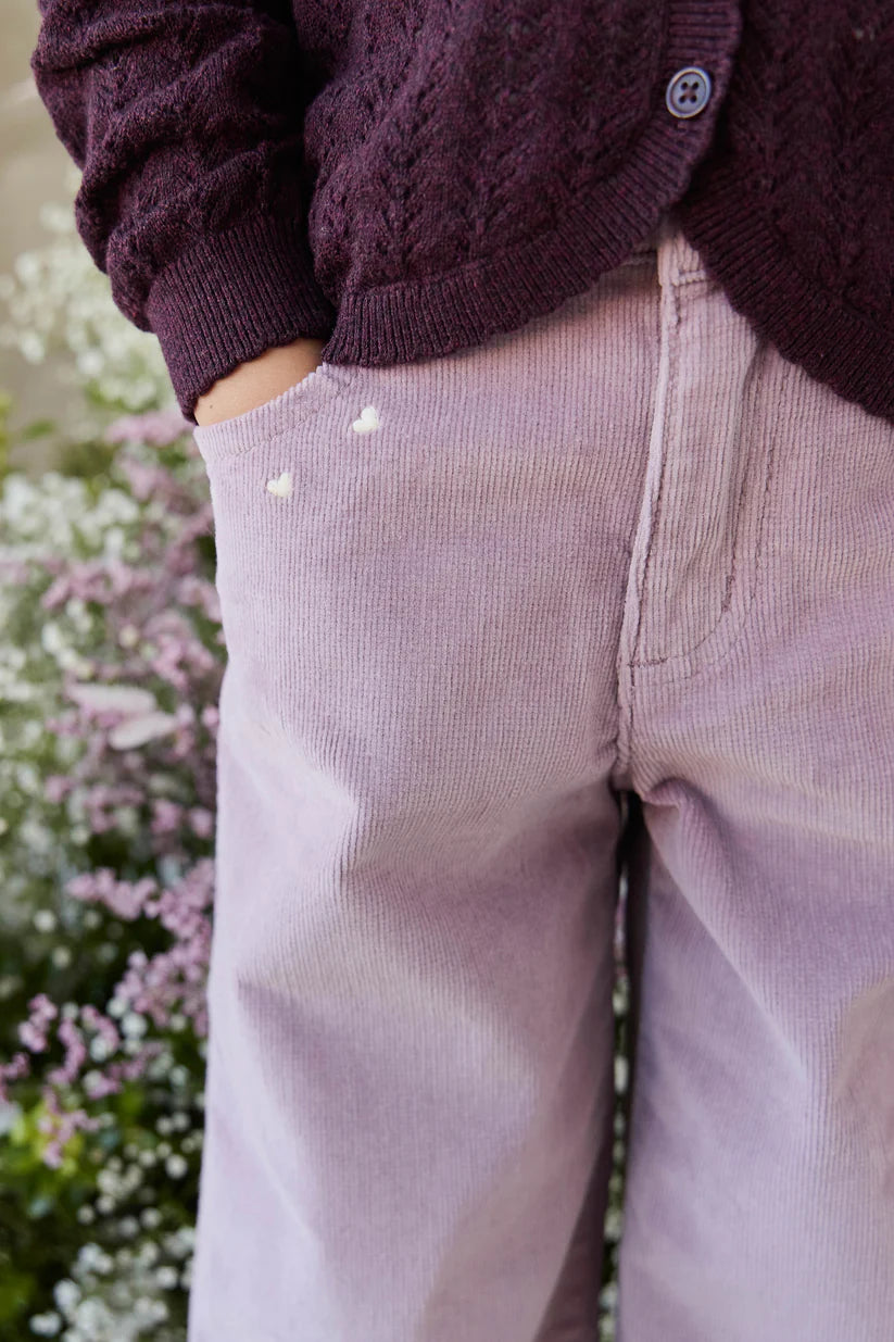 Person wearing a purple cardigan and light purple pants with a blurred floral background