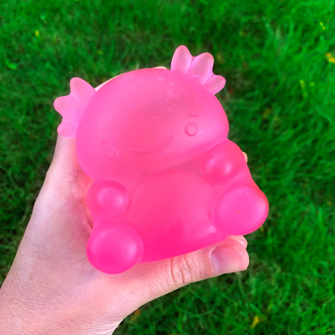 Pink rubber squish toy held in a hand with grass in the background