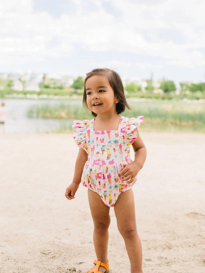 this picture shows the baby in a full picture of the romper with flutter sleeves and an ice cream print on the romper in pink , yellow and teal. 