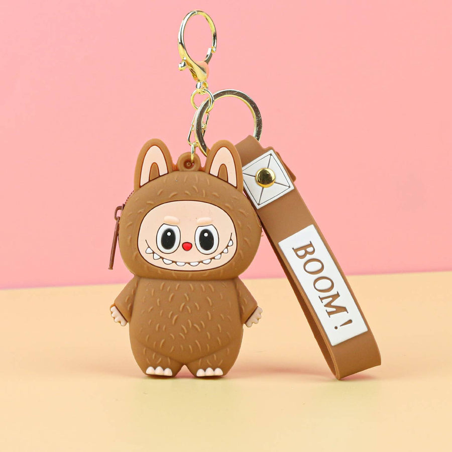 Cute brown plush charachter keychain with a strap labeled 'BOOM!' on a pink background