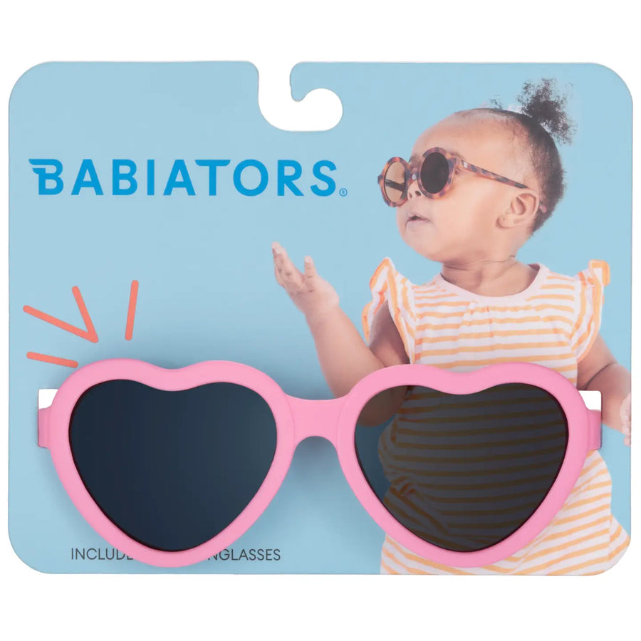 Heart-shaped sunglasses with pink frame on a Babiators packaging background
