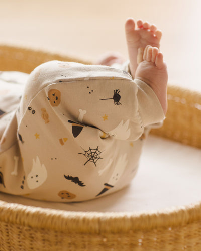 a close up of the print and colors in the jumpsuit, all neutral colors with an adorable spooky print: ghost, spider, witch hat, bat and pumpkin. This picture has the baby's feet kicking up in the air. 