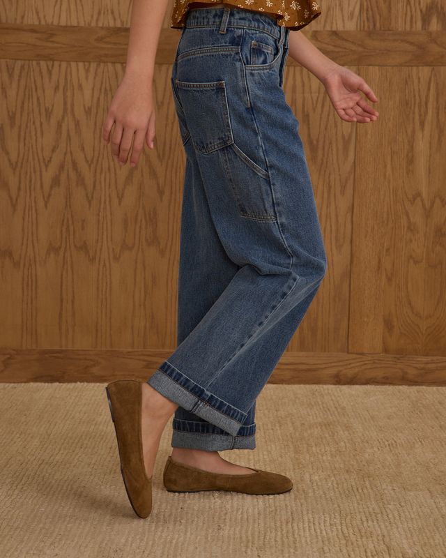 Person wearing blue jeans and brown shoes against a wooden panel background