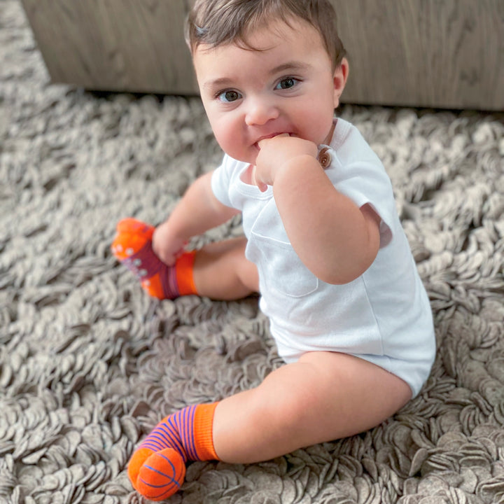baby wearing socks with basketballs attached to the toes. 