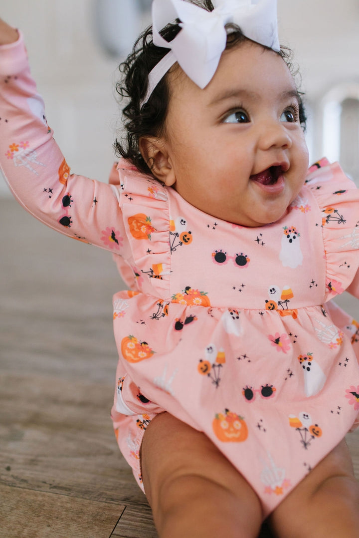 Baby wearing a pink floral onesie with a white bow on a wooden floor.