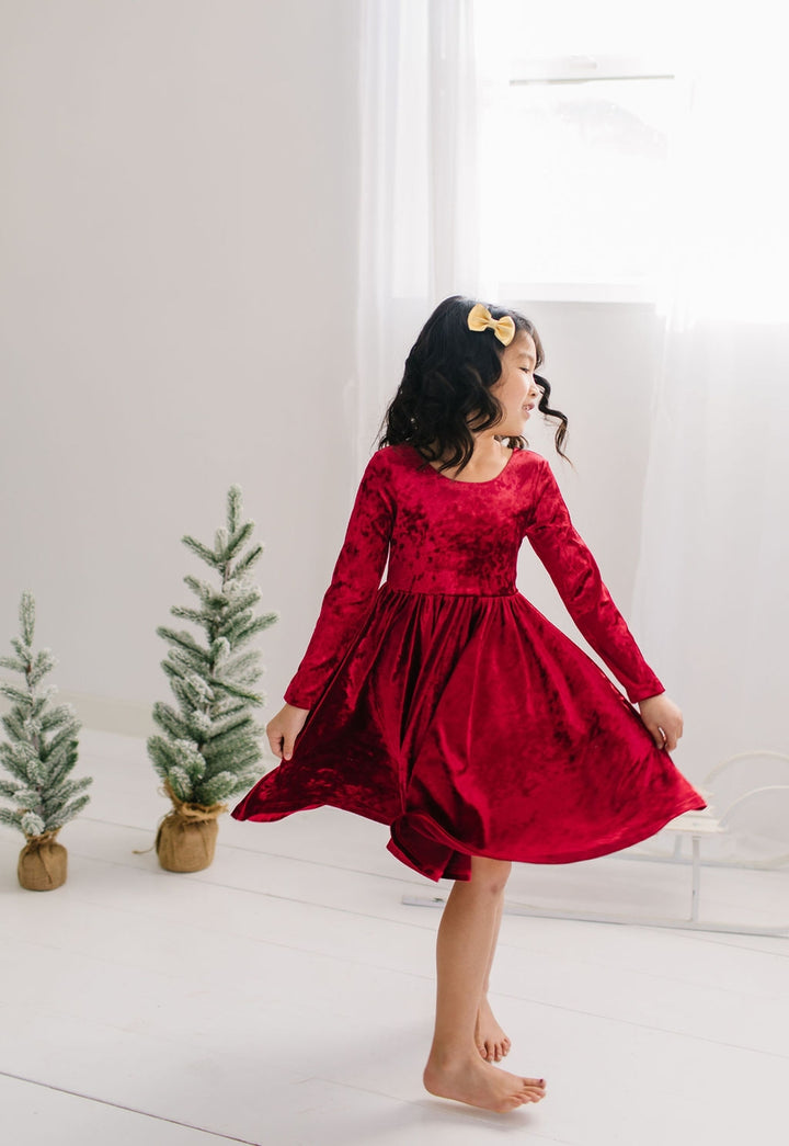 Child in a red velvet dress standing in a room with decorative trees.