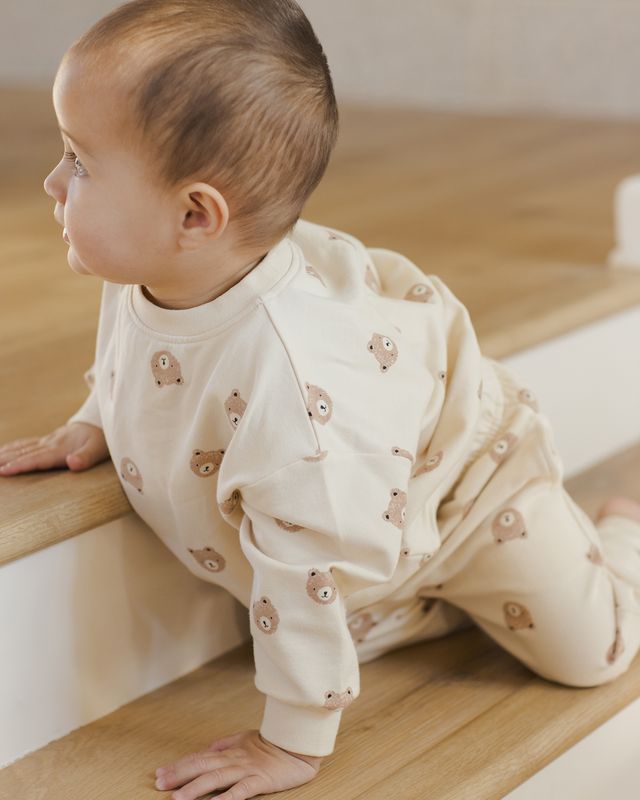 Baby in a cream outfit with bear patterns on a wooden floor