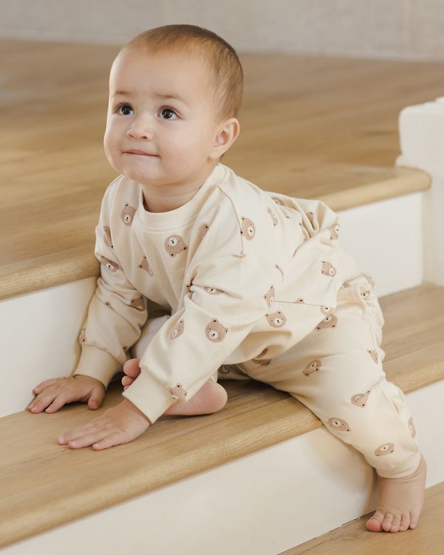 Baby in a beige outfit with floral patterns sitting on wooden stairs.