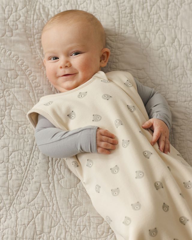 Baby lying on a textured surface wearing a white blanket with bear patterns