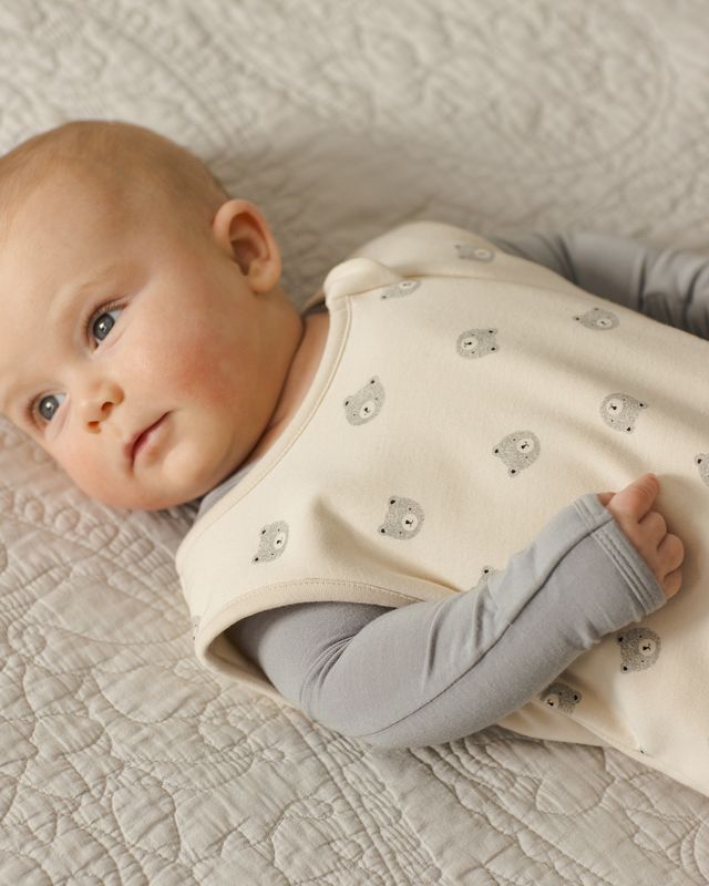 Baby wearing a cream-colored sleep sack with bear patterns on a textured surface