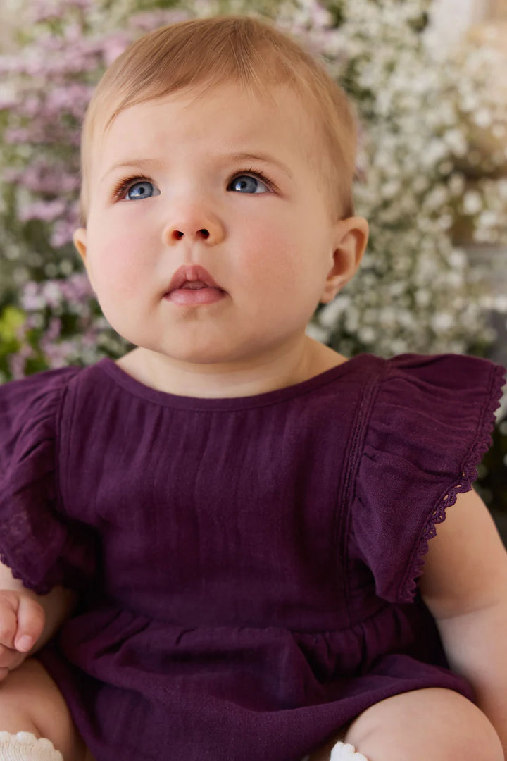 Baby in a purple romper sitting in front of floral background