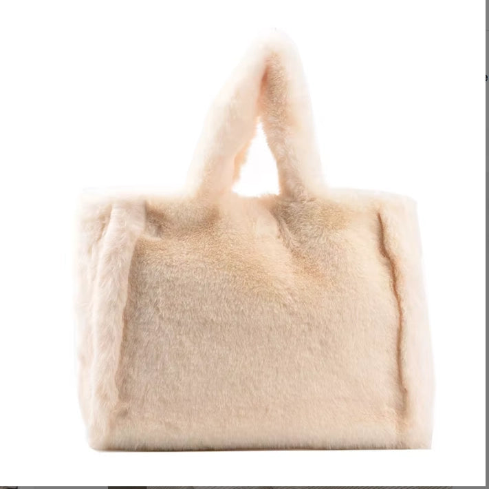 A soft, fluffy faux-fur handbag in a light cream or beige color, featuring two integrated top handles, shown against a plain white background.