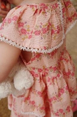 little girl modeling the pink frill with a look on how it fits at the shoulder and with the white trim. 