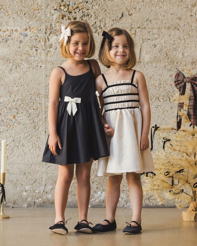 Two young girls in black and white dresses standing against a textured wall.