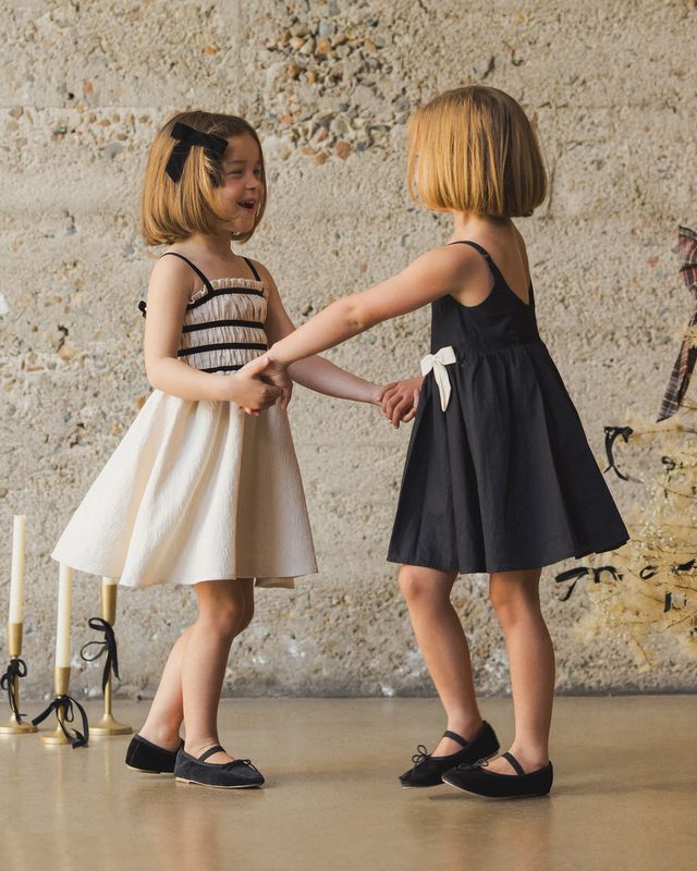 Two young girls in dresses holding hands against a textured wall.