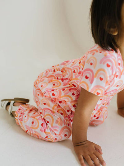 baby kneeling on the floor with an up close look at the print of the jumpsuit. 