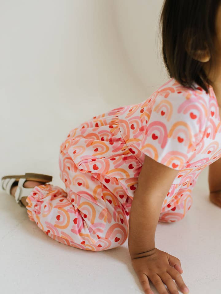 baby kneeling on the floor with an up close look at the print of the jumpsuit. 