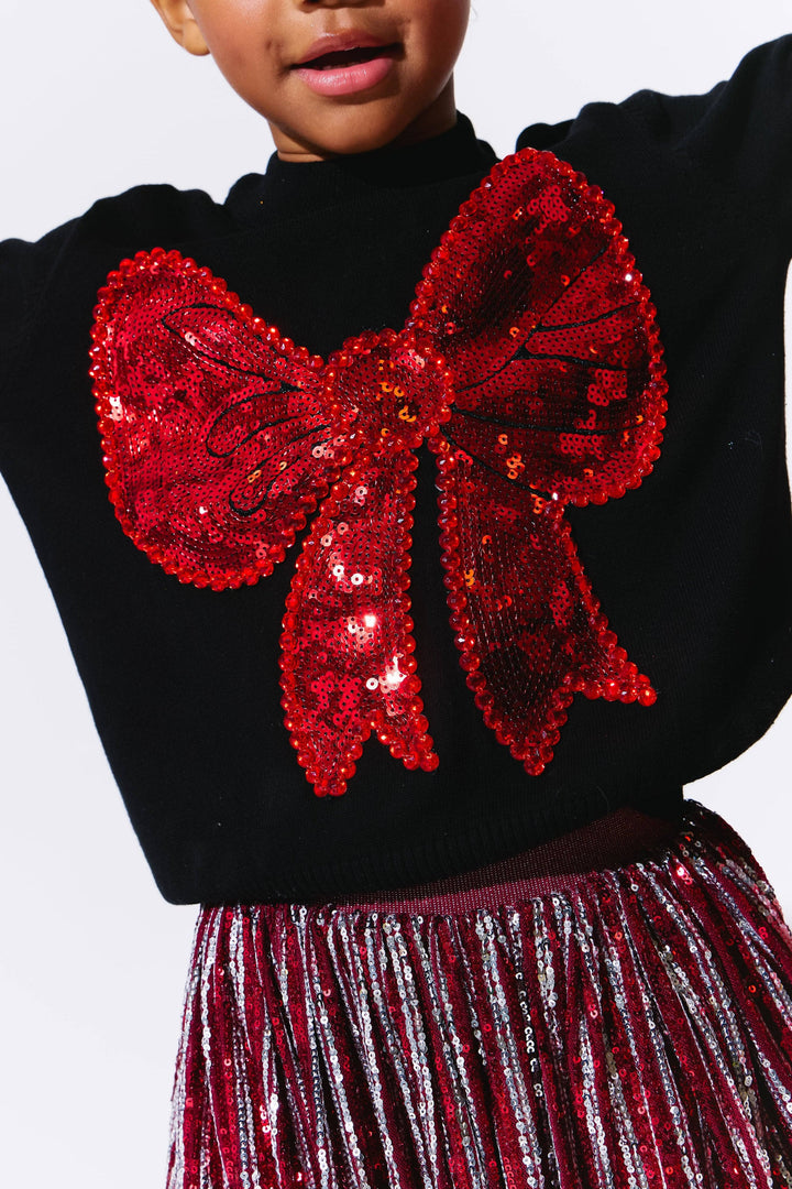 Black sweater with a large red sequin bow and red skirt on a white background