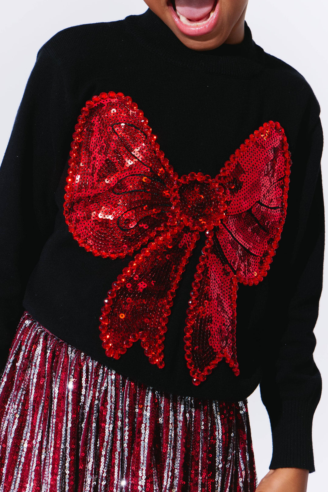 Black sweater with a large red sequin bow and a striped skirt.