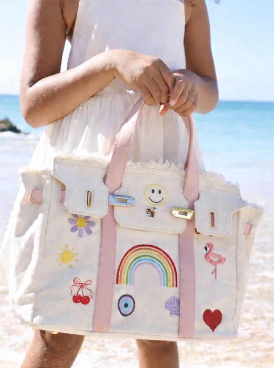 Person holding a colorful tote bag with cartoon designs on a beach.
