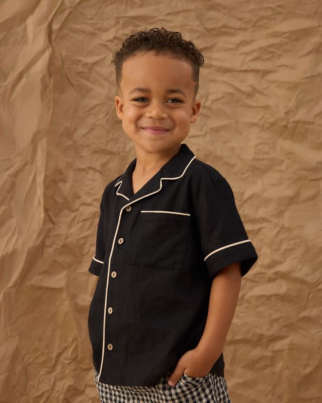 little boy wearing a black button with white piping 