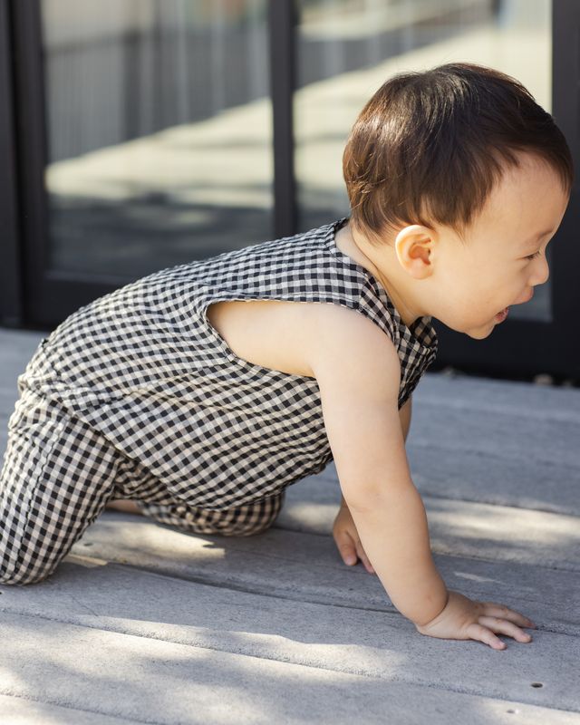 Baby in a black and white checkered outfit crawling on a wooden floor.