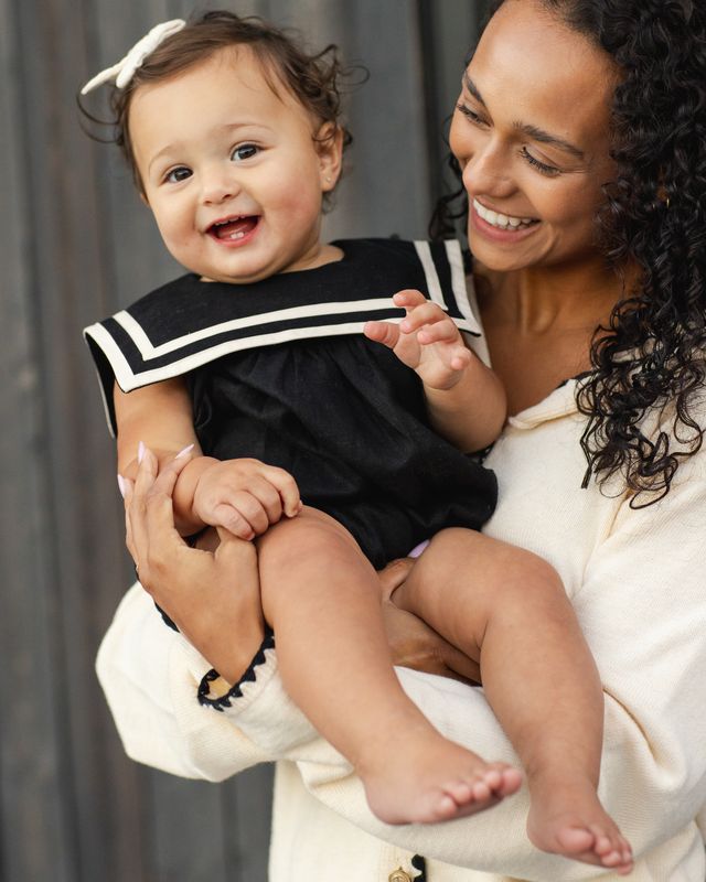 baby smiling and wearing a black sailor romper with white stripes. The baby is being held by her mom