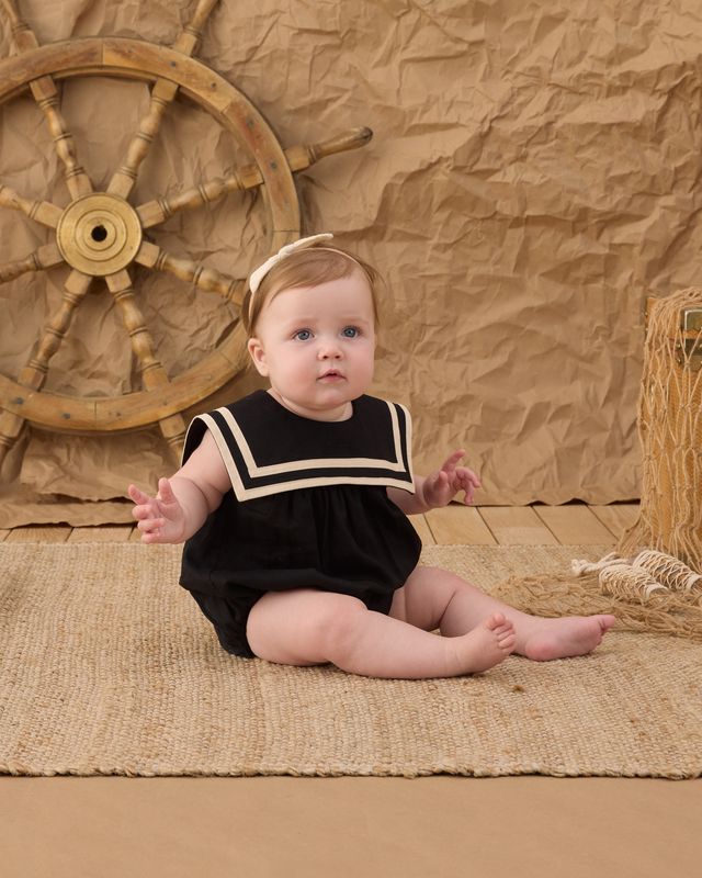 baby girl wearing black sailor outfit with white trim on the outfit. 