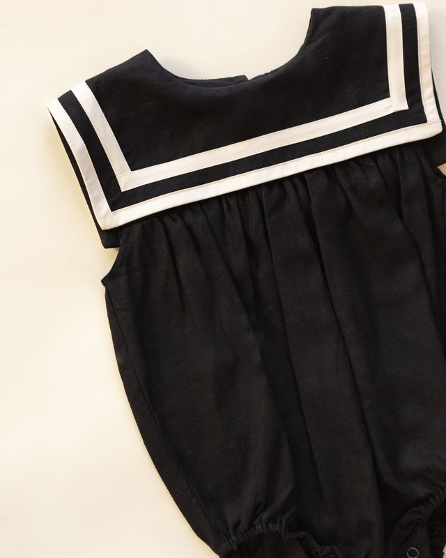 Black baby sailor outfit with white trim on a beige background