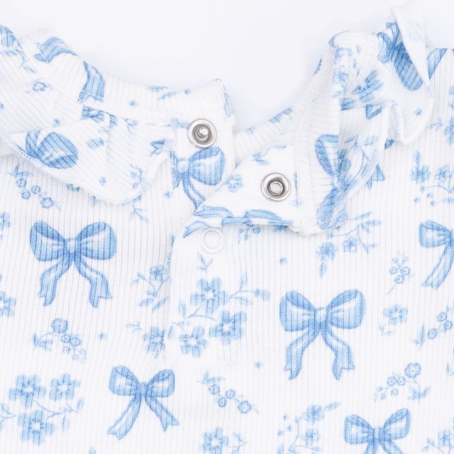 close up to the print and the snap closure at the top of the shirt. white base with blue bow and flower print. 