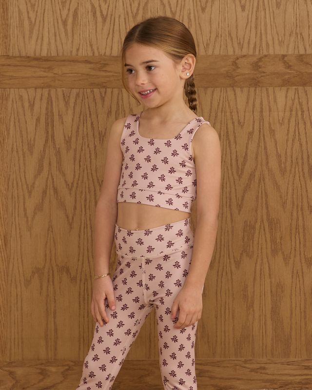 Young girl wearing a pink floral outfit against a wooden background