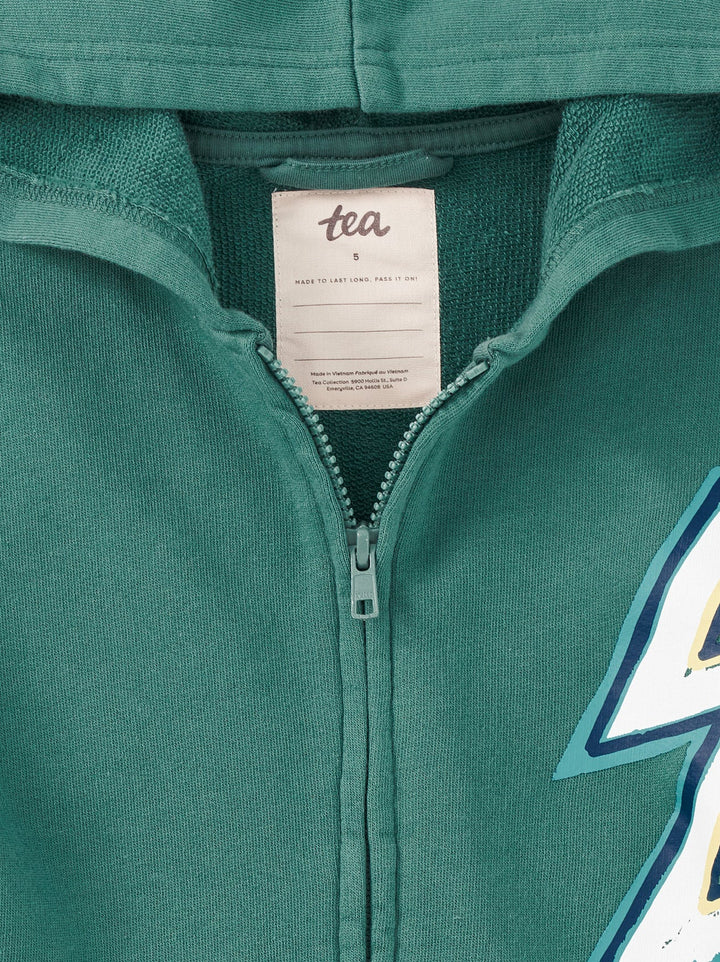 Close-up of a teal green zip-up hoodie showing the inner neck label with 'tea' printed on it, the zipper, and part of a graphic on the right side.