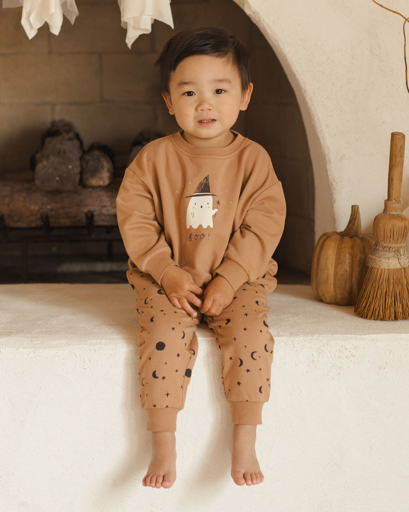 little boy modeling the halloween sweatsuit with a ghost on the sweatshirt and night sky print on the pants. 