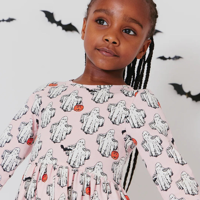 a little girl modeling the boo dress, long sleeve light pink dress with ghosts all over it. some ghosts are holding a pumpkin and others a bat