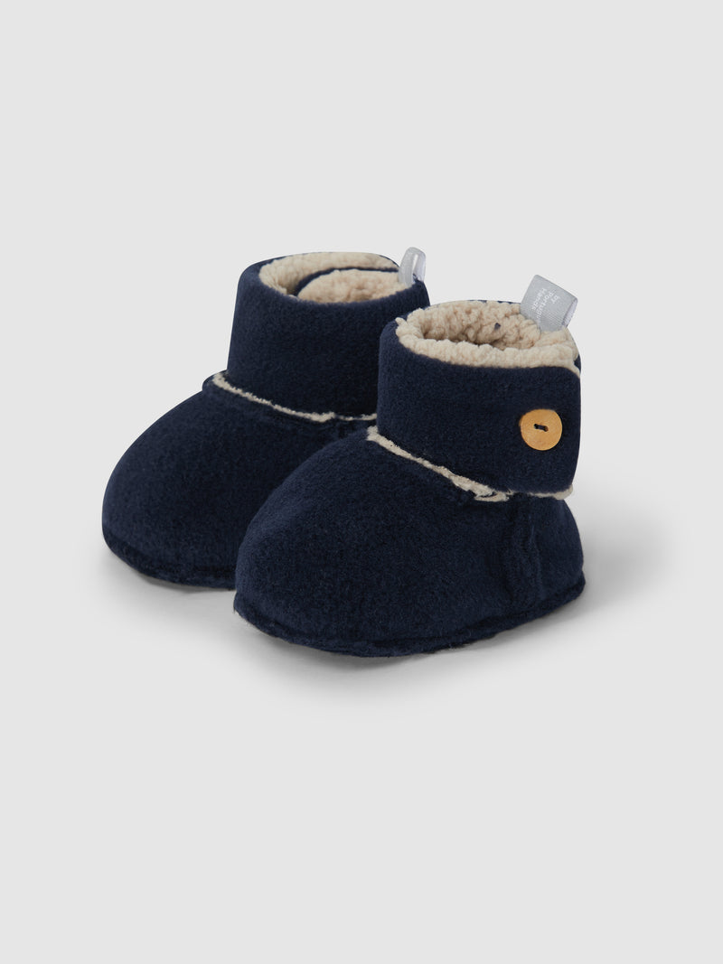 baby fleece lined booties fastened with a wooden button. navy in color with tan lining