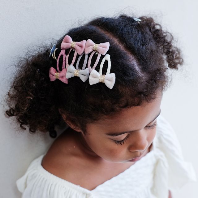 Child with curly hair wearing velvet  pink and white bow hair clips on a plain background