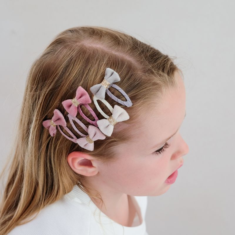 Child with colorful hair bows in their hair against a plain background