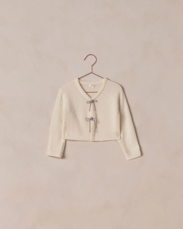 Cream-colored cardigan on a hanger against a beige background