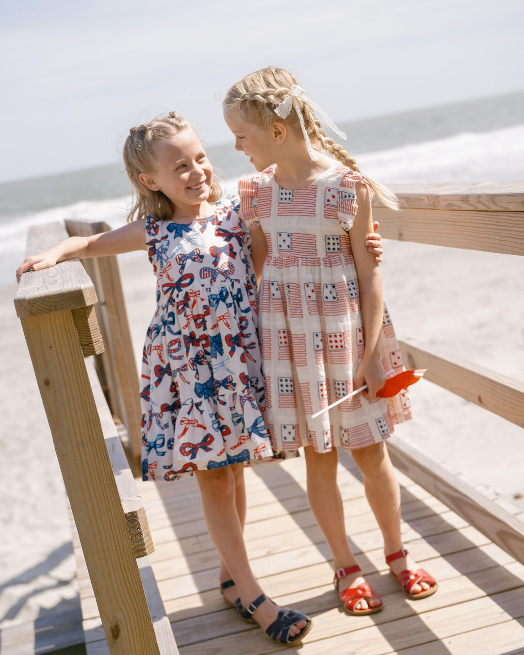 two little girls wearing summer dresses, one with bows all over it and the other with the american flag. 