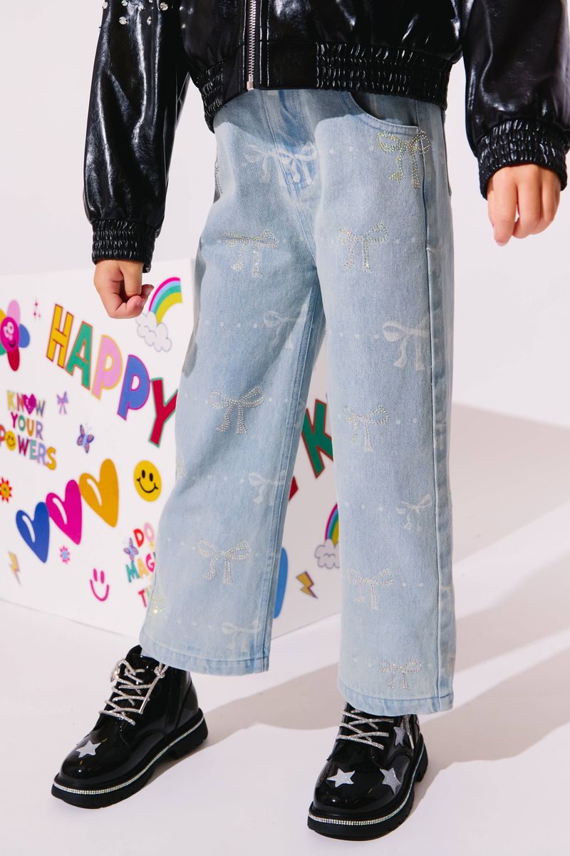 Person wearing light blue jeans with white patterns, black shoes, and a black jacket in front of a colorful background.