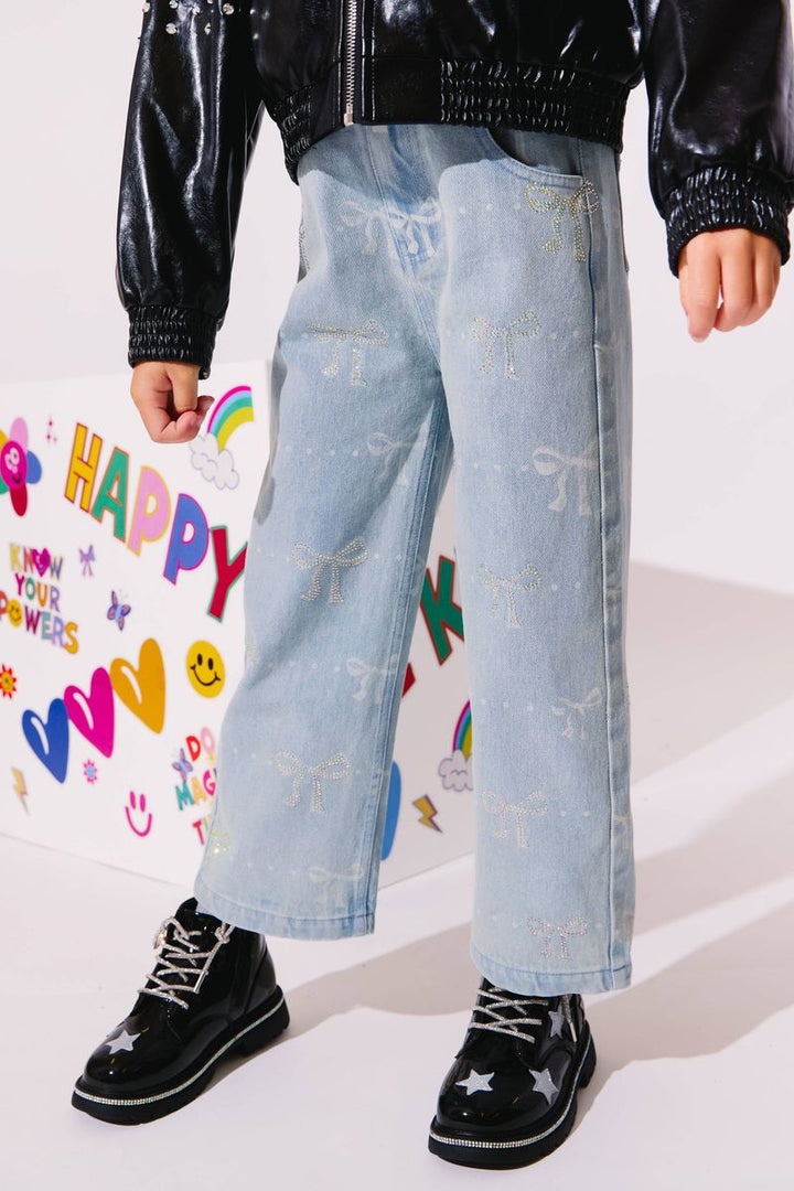 Person wearing light blue jeans with white patterns, black shoes, and a black jacket in front of a colorful background.