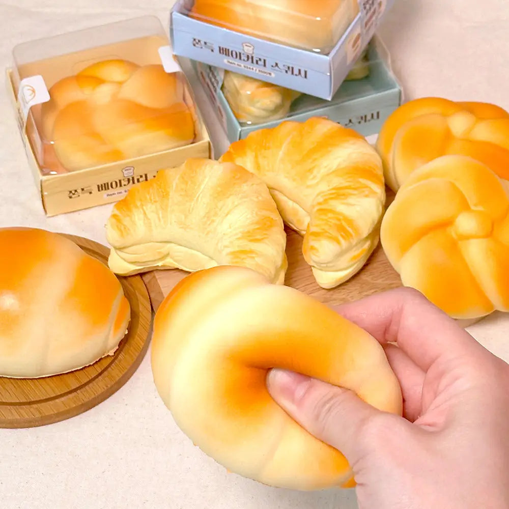 Hand holding a croissant-shaped bread with more bread items in the background on a neutral surface.
