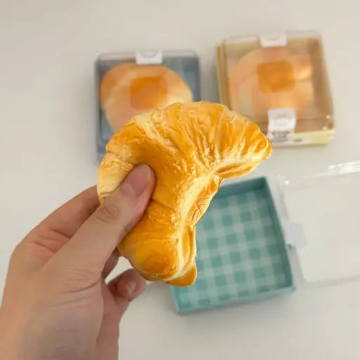 Hand holding a croissant-shaped bread toy with packaged croissants in the background.