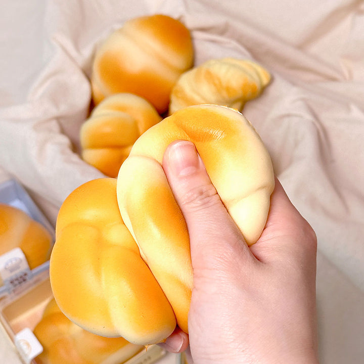 Hand holding a soft, yellow bread-like toy with more toys and a box in the background.