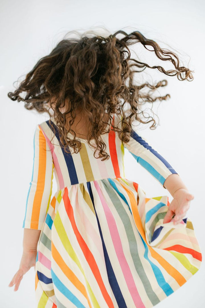 Child wearing a colorful striped dress with long, curly hair on a white background
