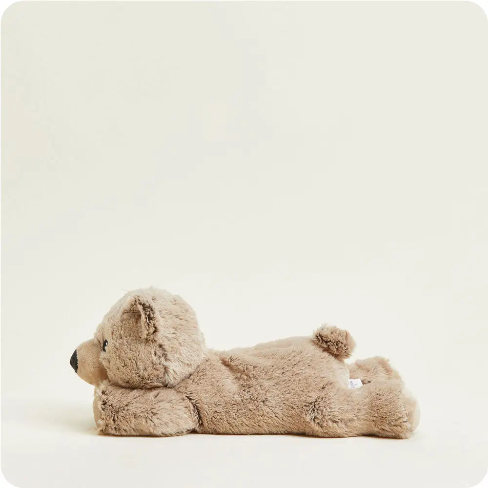 A plush teddy bear toy lying on its side, photographed against a plain warm off-white studio background.